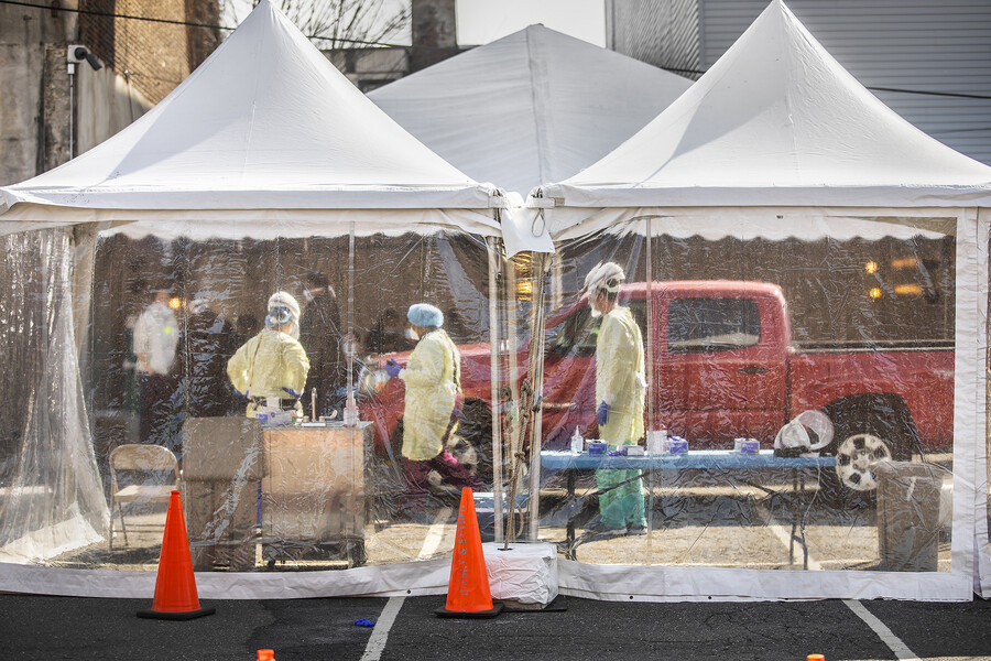 pop-up tents at COVID-19 testing site with medical personnel attending to a driver in a pickup truck