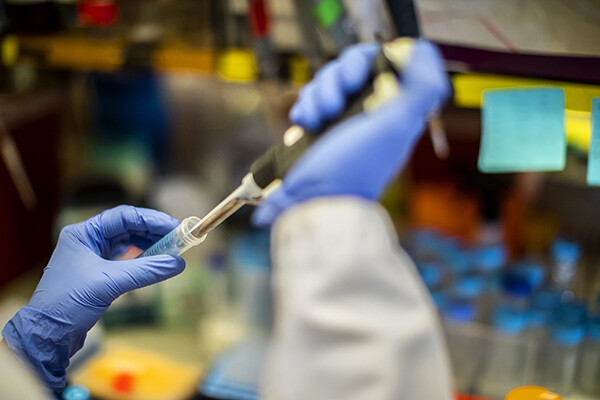 Two gloved hands hold a syringe and needle in a lab setting