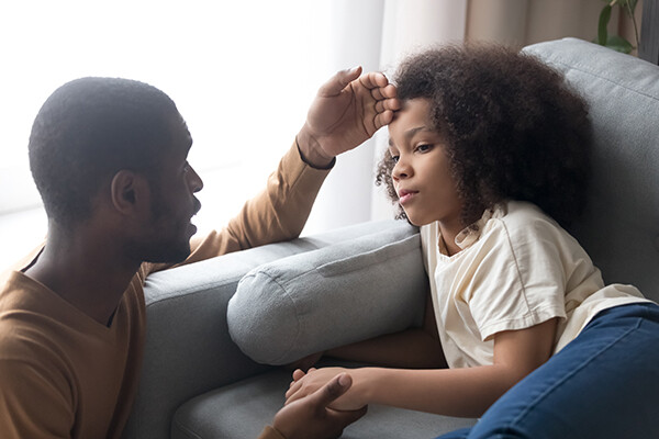 Concerned parent holding an adolescent child's hand and touching their forehead