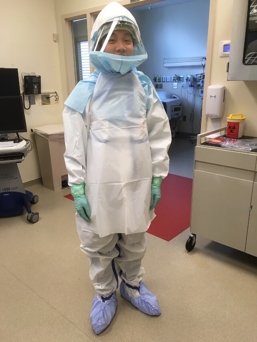 Alex Chen stands wearing biohazard suit, gloves and mask.