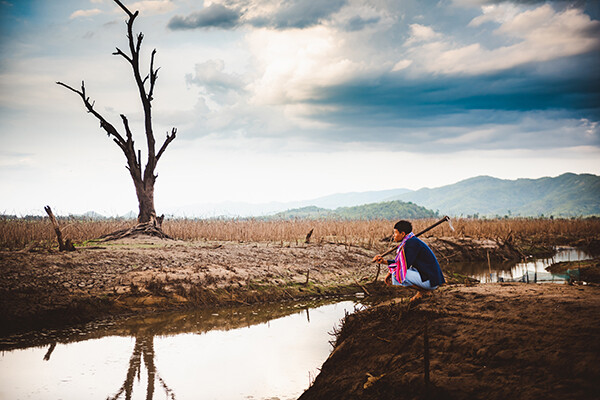 farmer sits on cracked earth near drying water source