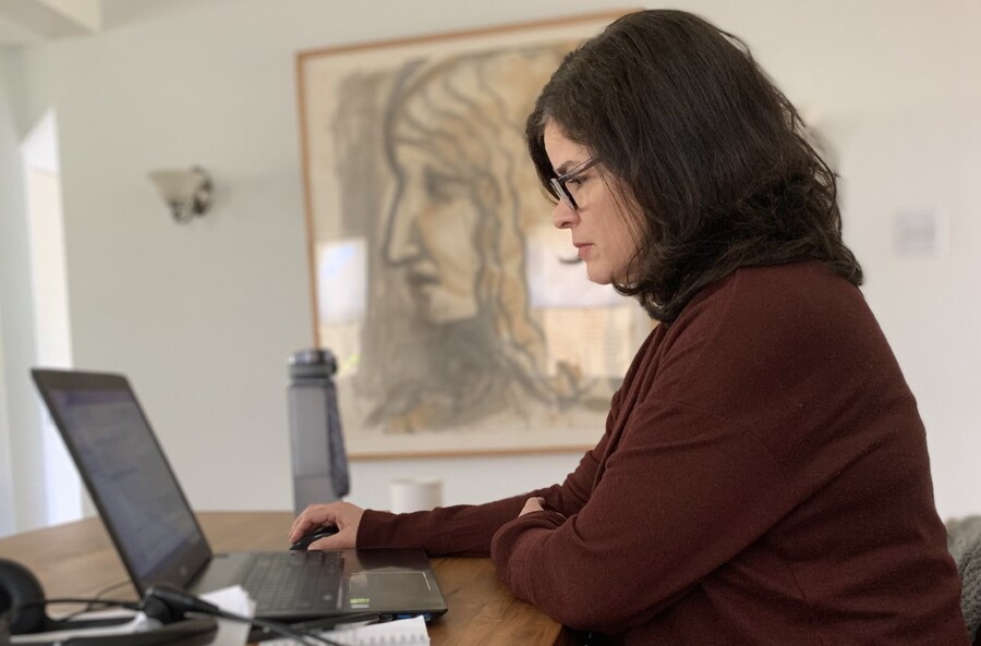 Librarian sitting at a table pictured in profile working on a laptop with a large work of art in profile in the background.