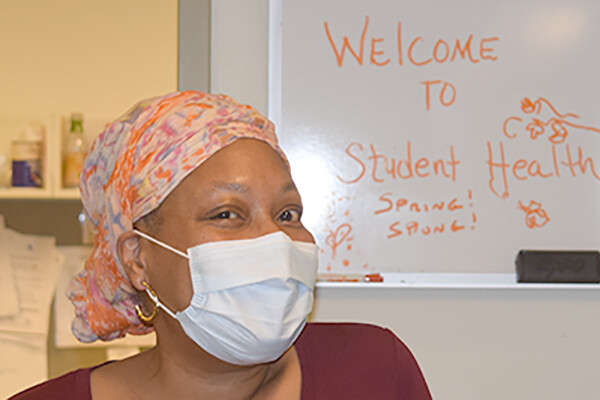 Cassandra Adams wearing a medical mask and scarf on her head stands in front of a white board