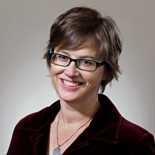 A close up headshot of a smiling person with short brown hair and glasses. 