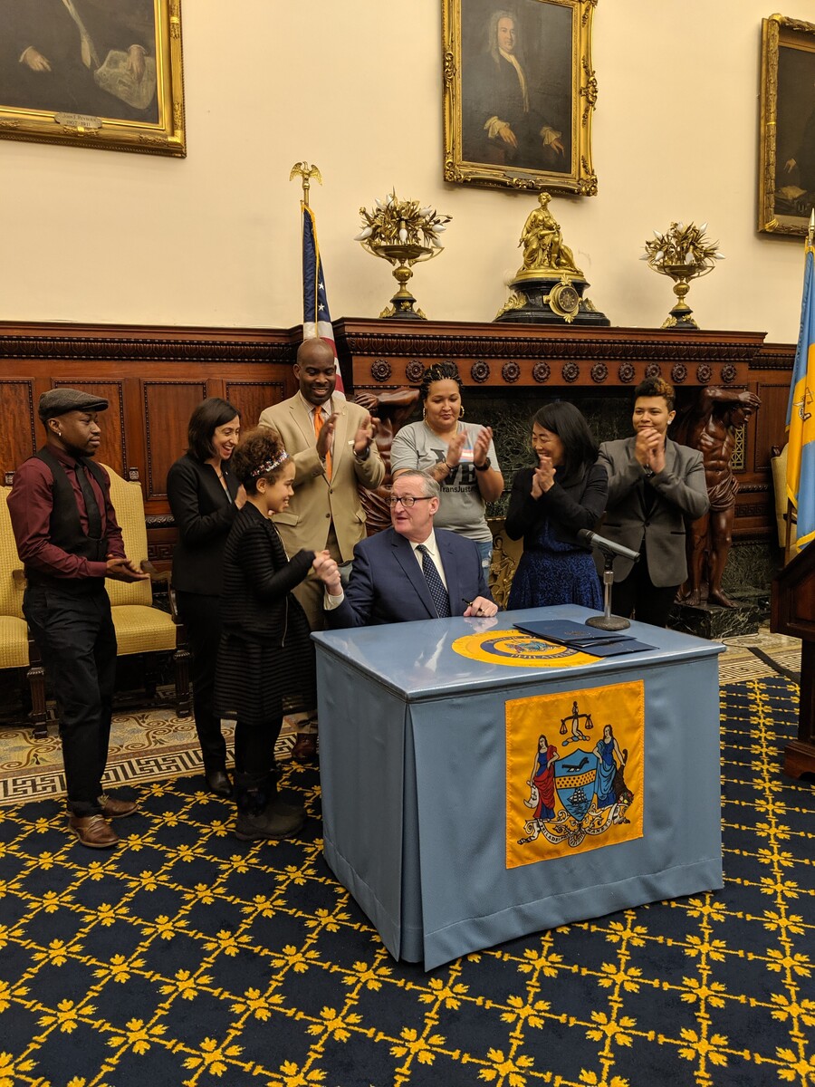 Mayor Kenney shakes a young woman's hand as 6 people behind him clap