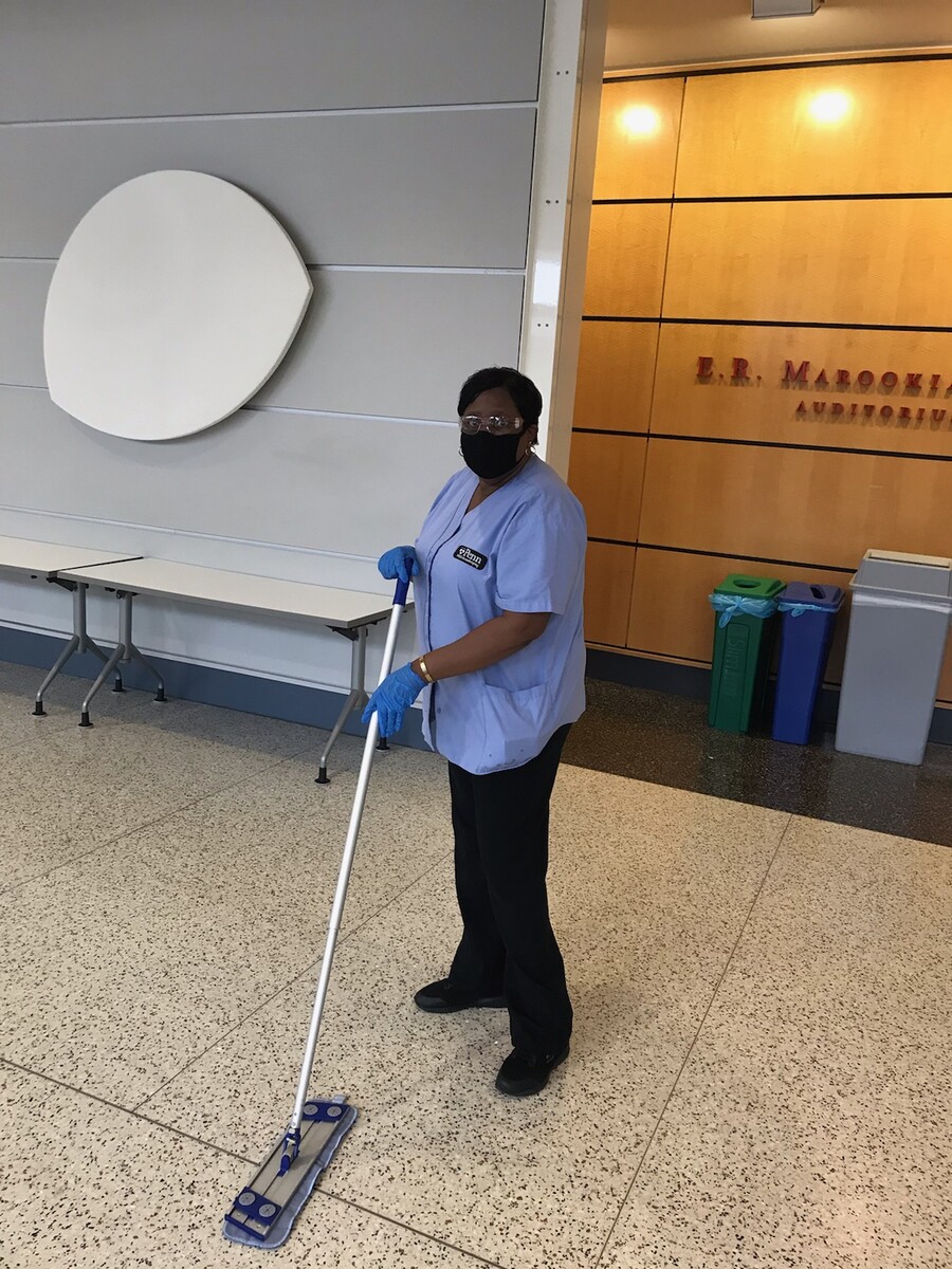 Woman in mask and gloves cleans the floor in front of an auditorium
