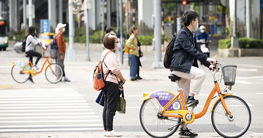 Pedestrians and bicyclists at a crosswalk wearing face coverings in a Taiwanese city.