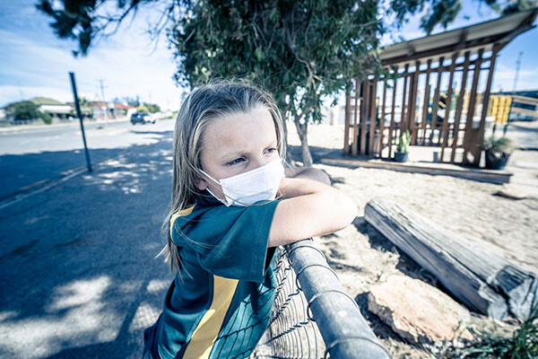 adolescent wearing face mask leans on fence staring into distance