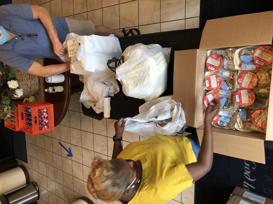 People putting food into plastic and paper bags from a table. Another table behind them houses crates of other food.
