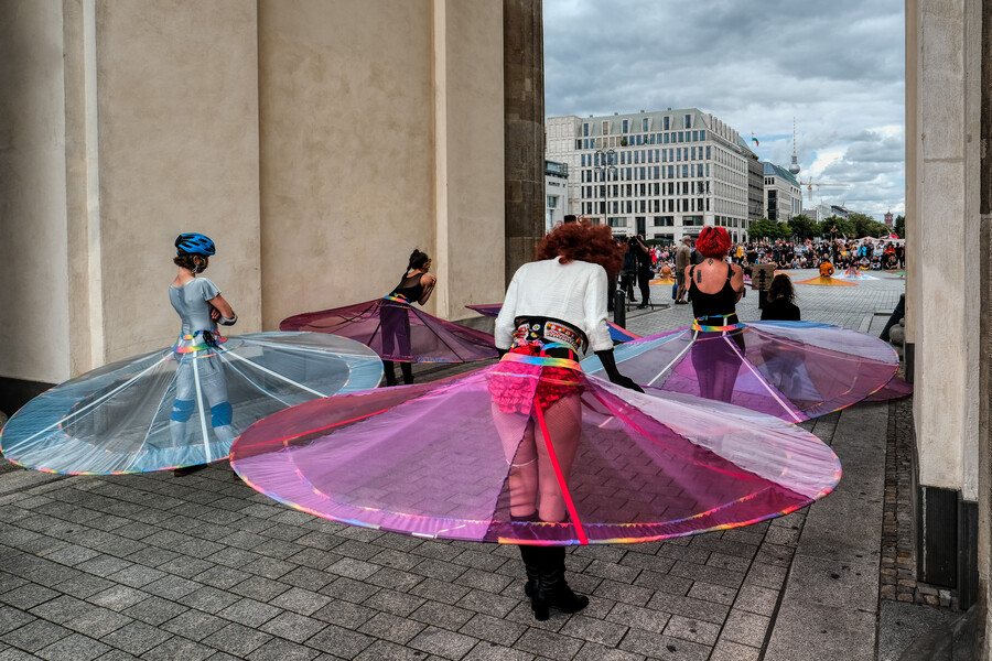 people standing under the brandenburg gate with large hoop skirts to indicate social distancing measures
