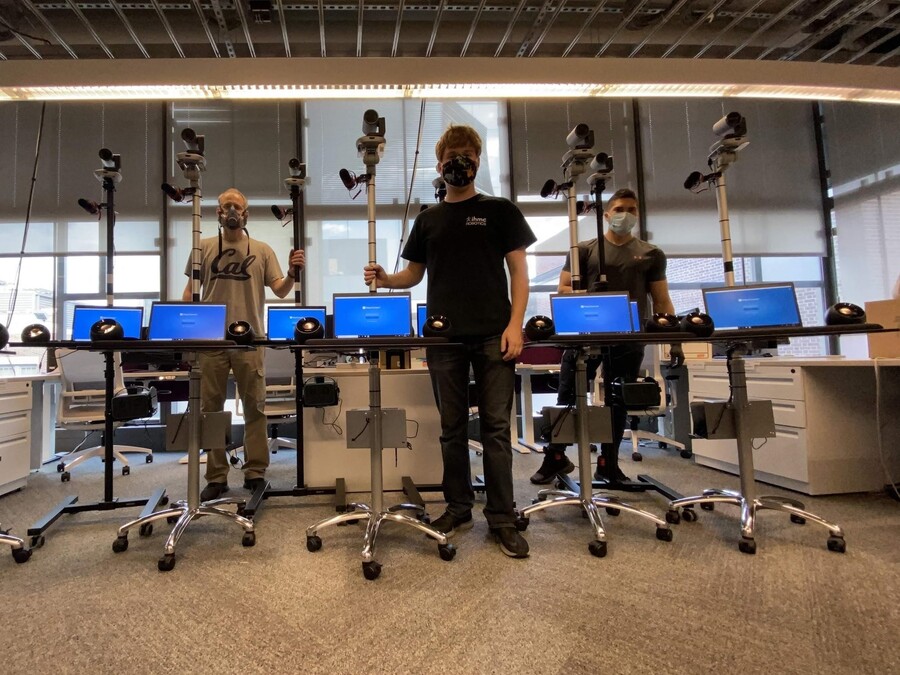 three people in an office standing next to telemedicine carts, with laptops, cameras, and speakers on a rolled cart
