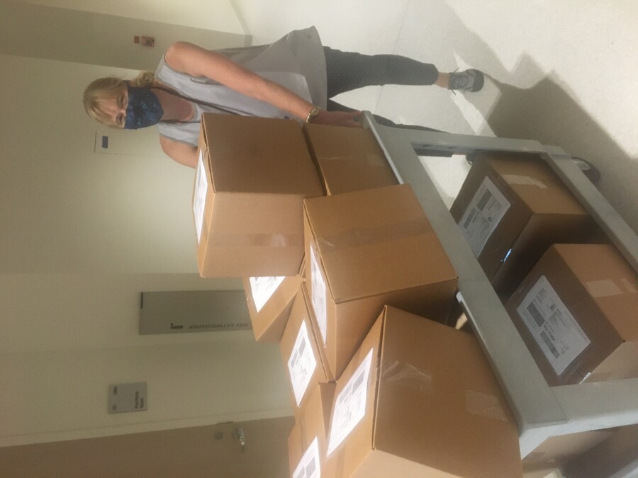 Person in mask pushes cart full of boxes in hallway