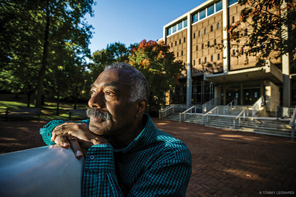 Ancil George leans on The Button sculpture in daylight in front of Van Pelt Library.