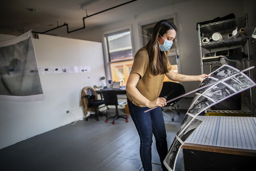 Amrita Stützle holds a large sheet of prints while wearing a mask in her studio.