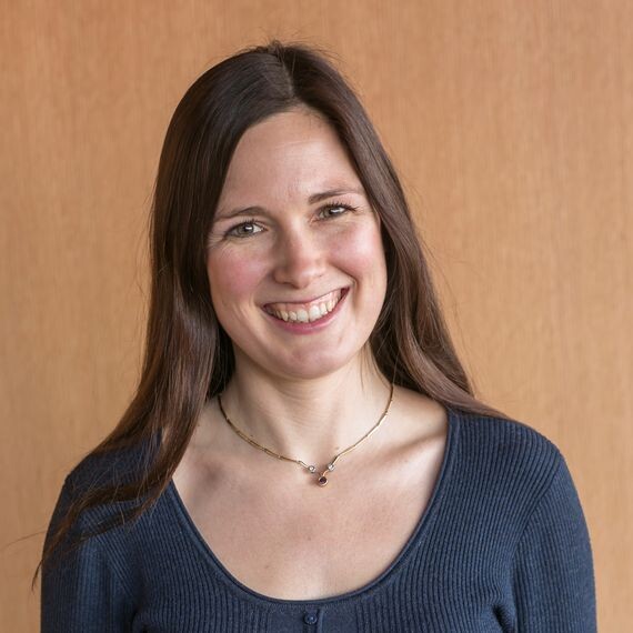 Up close photo of a person smiling, wearing a blue shirt and a gold necklace. 
