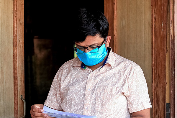 Person wearing a face mask stands outside their door looking at an eviction notice in their hand.