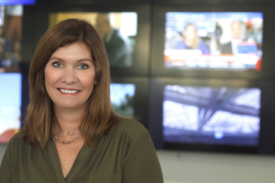 Sarah Banet-Weiser smiling in front of a wall of computer screens.