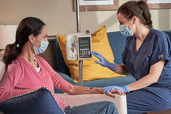 Person wearing a face mask seated in a chair receives and IV drip from a nurse wearing a face mask.
