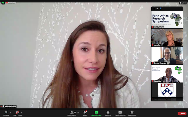 A woman with long straight brown hair in a white shirt with off white background with white flowers talks on a Zoom call as five other Zoom participants' screen are stacked vertically on the right side of the screen