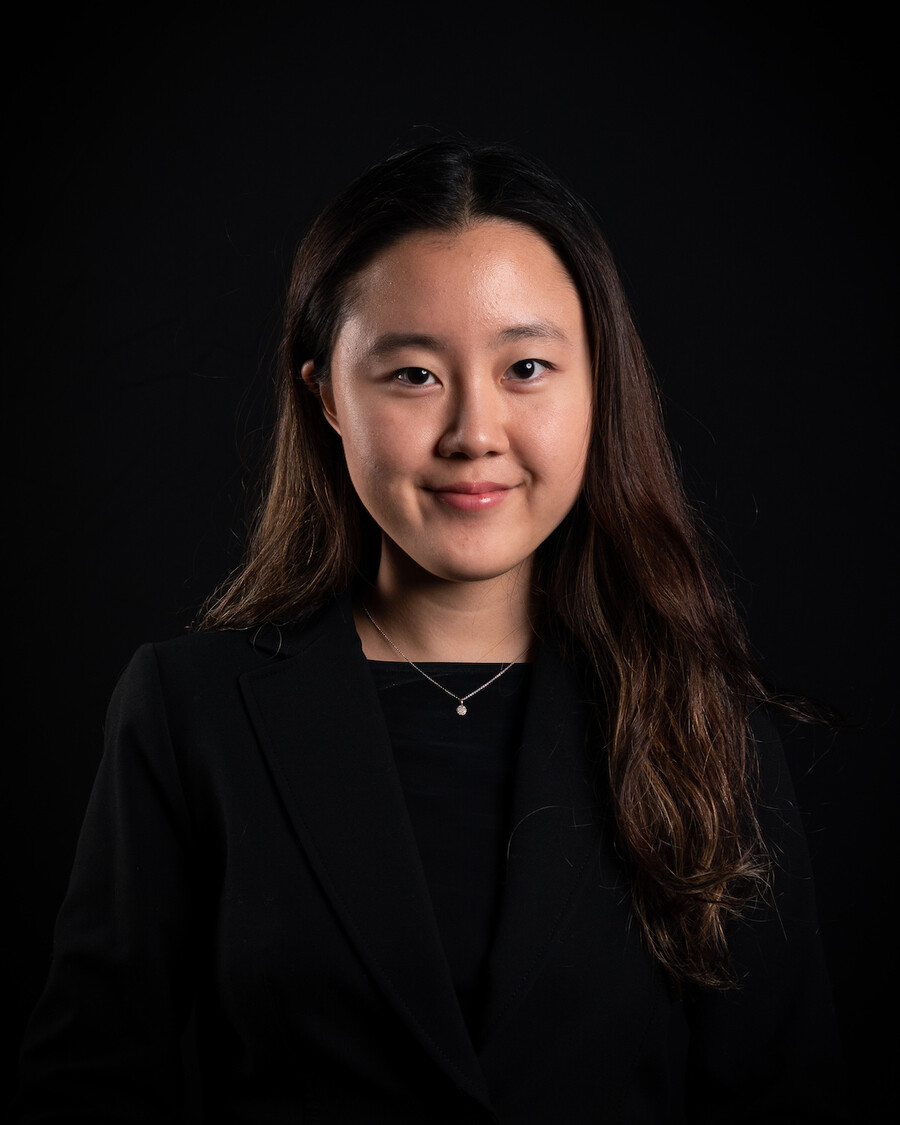 Woman with long brown hair in black shirt with black background smiles at the camera