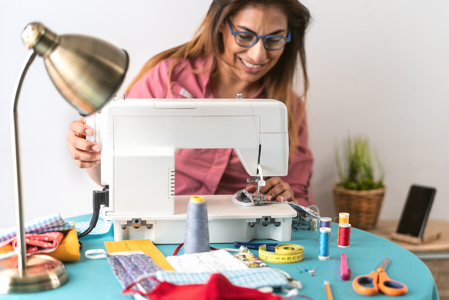 Person smiling at a sewing machine while making masks for COVID-19 face coverings.