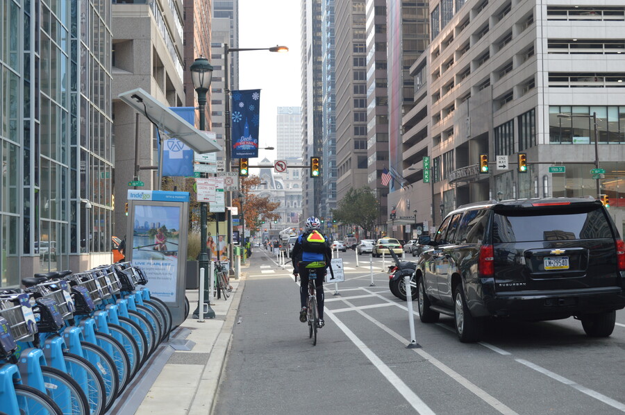 a person biking down a bike lane in a city with a sidewalk on one side and cars on the other