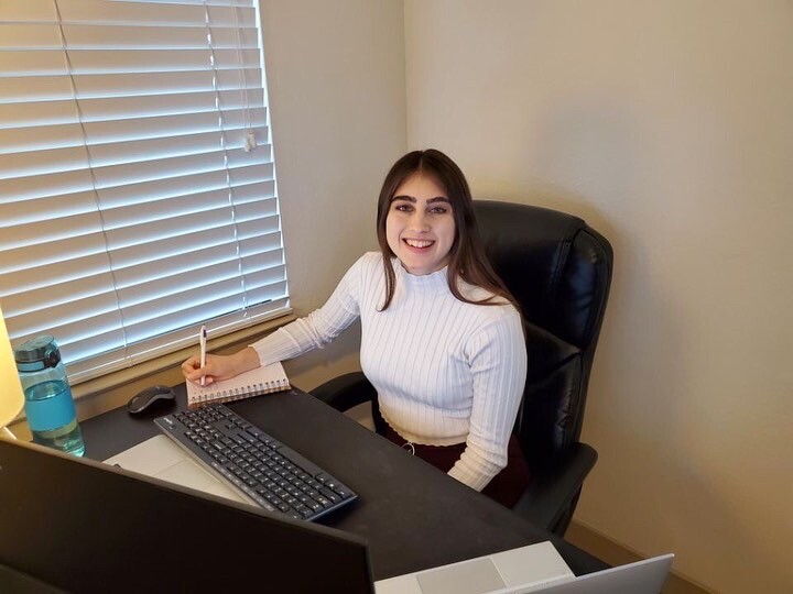 Smiling student at a computer with a notebook and pen in hand