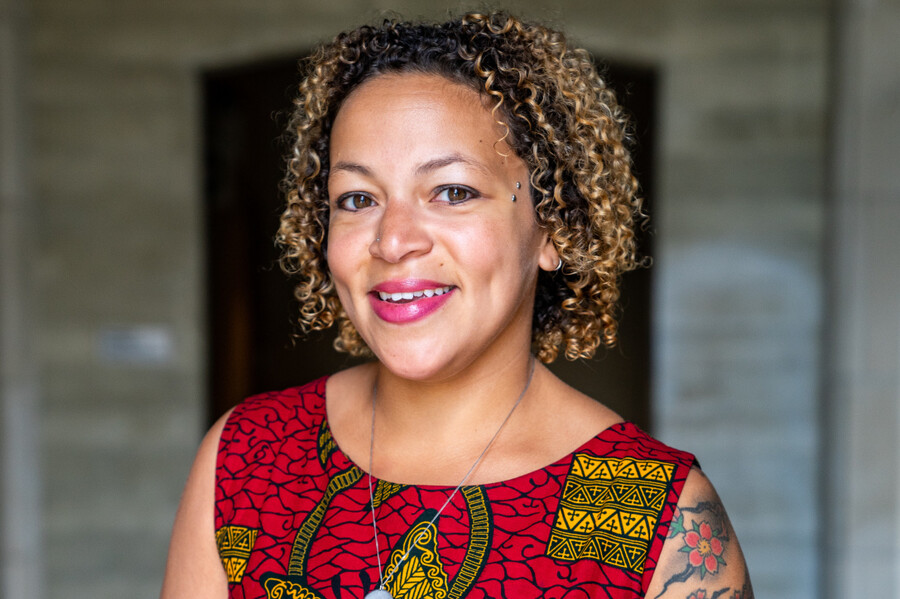 The top half of a person standing outside, background blurred, wearing a red patterned dress with a silver necklace and red lipstick.