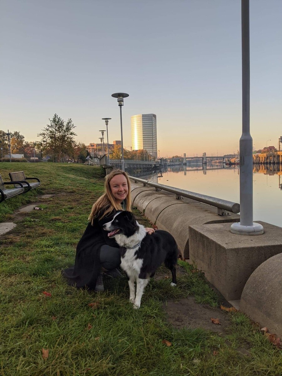 Person kneels with a large black and white dog along a riverbank