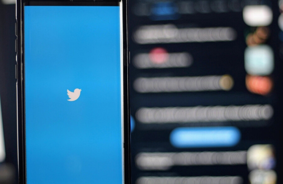 Smart phone with Twitter logo in front of a blurry computer screen in the background.