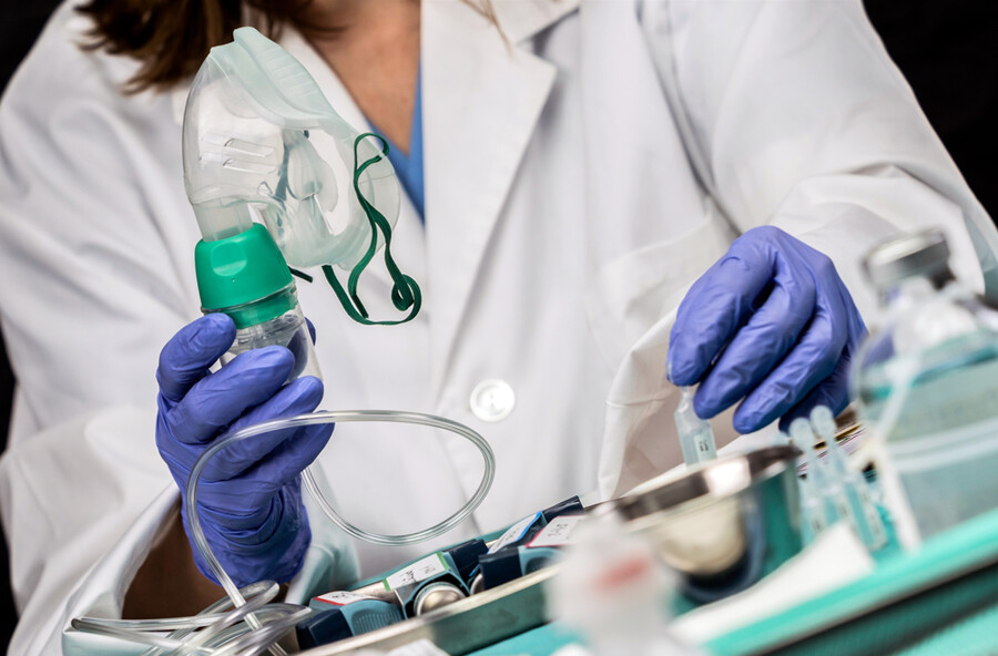 Doctor wearing a white coat and latex gloves holds up an oxygen mask.