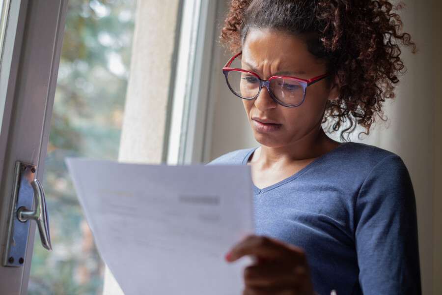 Concerned person standing by a window looking at a sheet of paper.