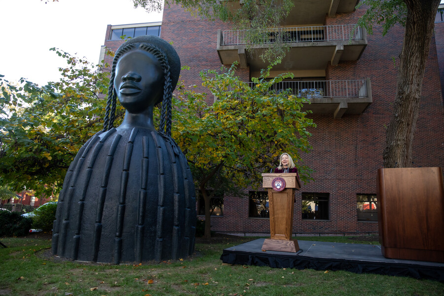 Amy Gutmann at podium, with towering sculpture to her left