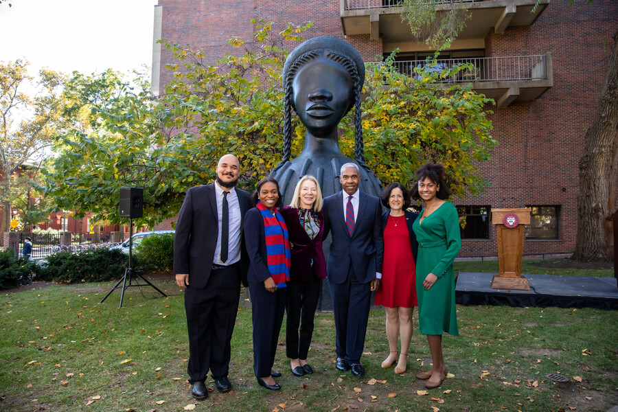 Group stands in front of Brick House sculpture. Speaker to the people's right and podium to their left.