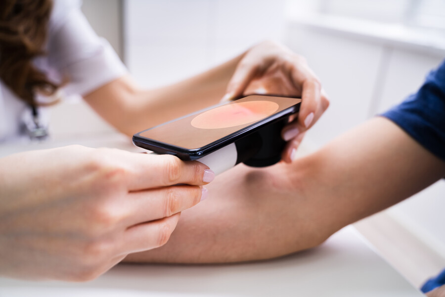 Medical professional looking closely with a smartphone lens at pigment on a person’s arm.