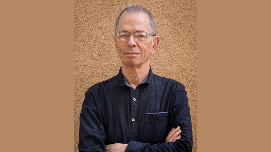 Peter Sterling standing arms crossed in front of a tan textured wall. 