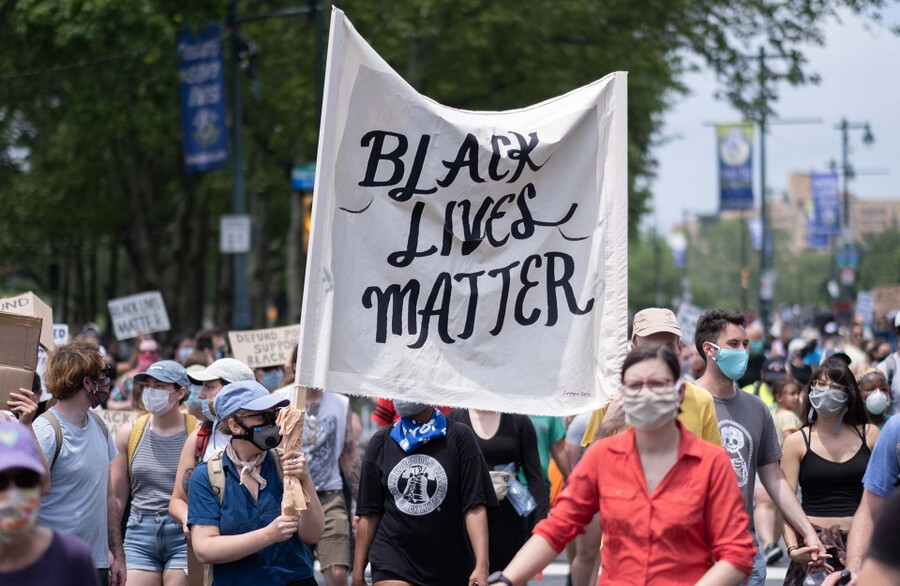 Group of protesters in masks in the streets, one carries a large sign that reads BLACK LIVES MATTER.