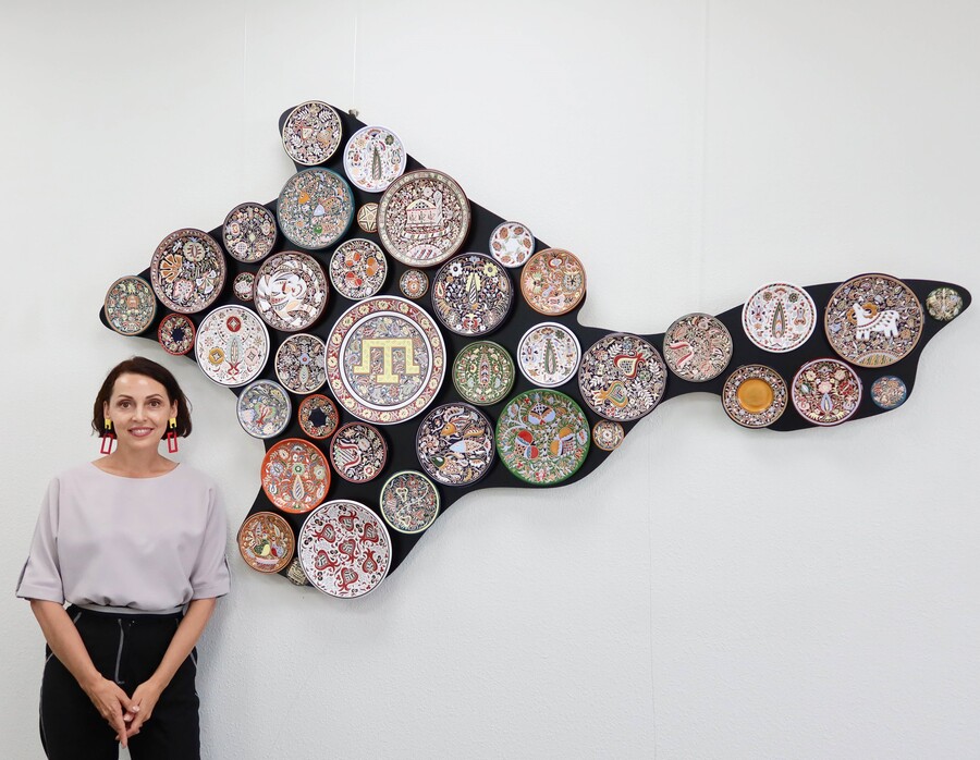 A person standing in front of an art installation made up of very colorful places on a black background in the shape of a map.
