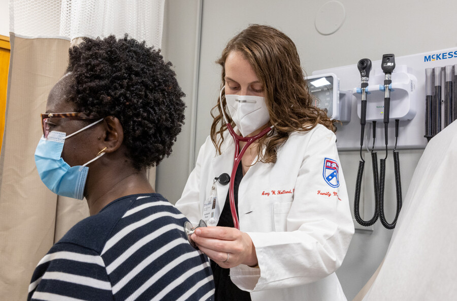 A doctor with a stethoscope checks a patient’s back heartbeat.