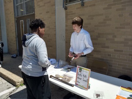 One person gives another person information at a table with a sign that says "Let's talk about Lead"