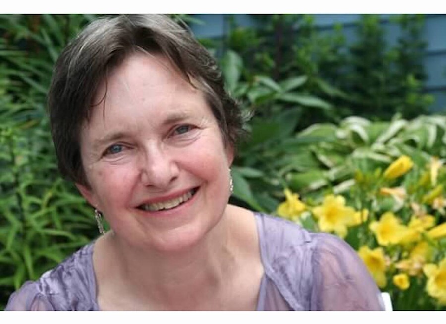 Mary Summers smiles for the camera in front of a green plant with yellow flowers