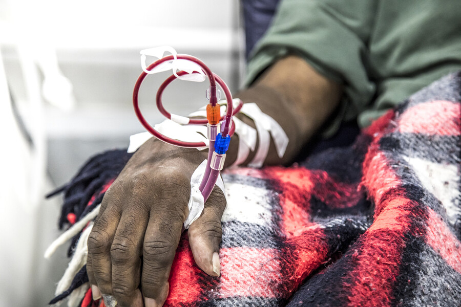 African American person at a renal clinic with a blanket on their lap and an IV in their hand.