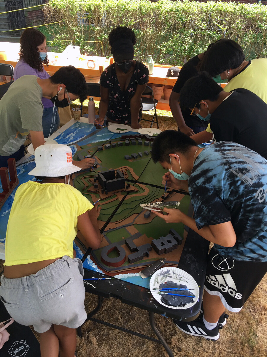 A group of teenage students working on a table scale model.