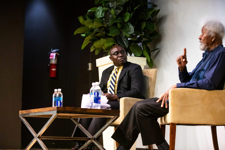 Wale Adebanwi seated and speaking on stage with Wole Soyinka.