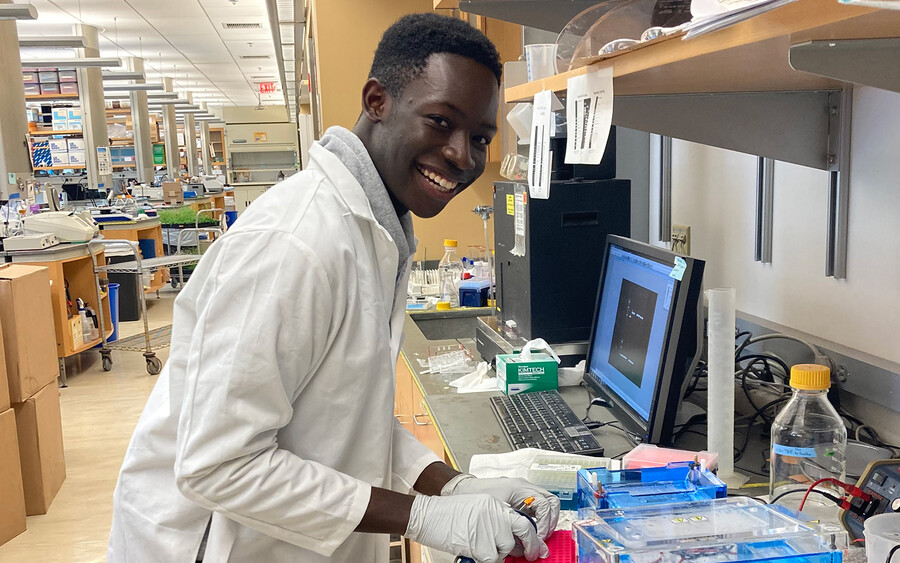 A student smiling in a lab wearing a lab coat.