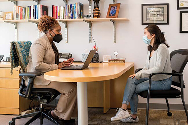 Andrea Kane (left) sits at a desk with a laptop opposite a student in her office.