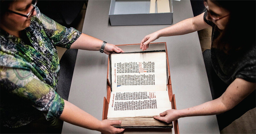 Dot Porter (left) and Andrea Nunez hold a rare book on a table.