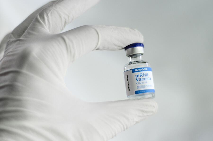 A gloved hand holding a small vial of Sars-CoV2 mRNA vaccine.