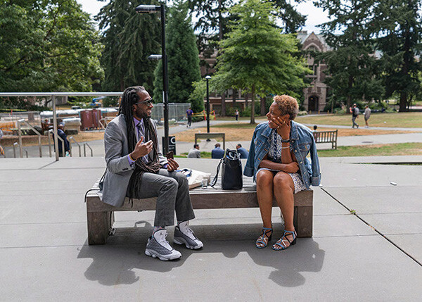 Two people sit outside on a bench talking