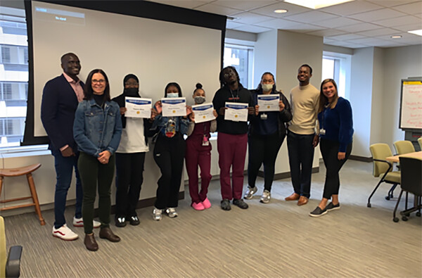 Students and four advisers in a conference room, the five students hold up certificates.